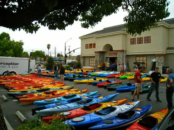 Many colorful whitewater kayaks of various shapes and sizes parked in front of a building.