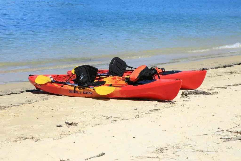 Two red kayaks sitting on the sand next to a body of water.