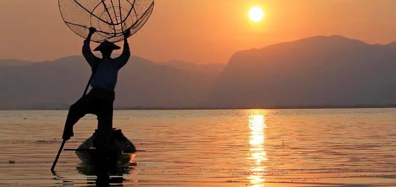 A man in a kayak holding a fishing net at sunset, focusing on stability.